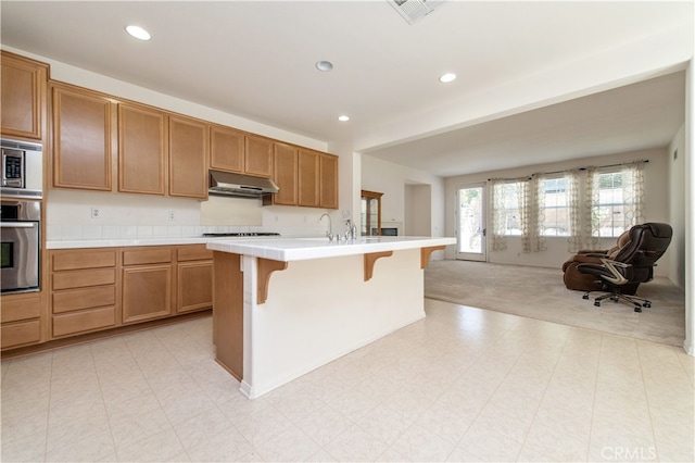 10324 Bold Red Dr, Rancho Cucamonga, CA 91730 - kitchen featuring stainless steel appliances, under cabinet range hood, open floor plan, a kitchen bar, and recessed lighting