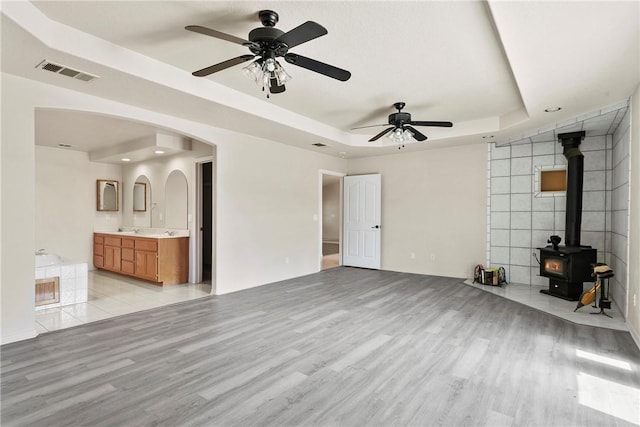 8379 Beaver Ave, Phelan, CA 92371 - unfurnished living room featuring a tray ceiling, light wood finished floors, ceiling fan, a wood stove, and arched walkways