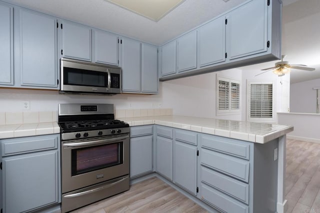 28328 Via Bandita, Menifee, CA 92585 - kitchen with appliances with stainless steel finishes, a peninsula, light wood-type flooring, and ceiling fan
