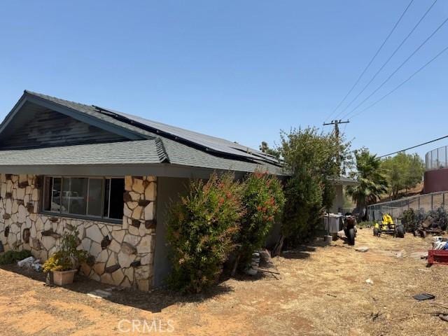 2089 Monterey Peninsula Dr, Corona, CA 92882 - view of side of property featuring stone siding, roof mounted solar panels, and a shingled roof