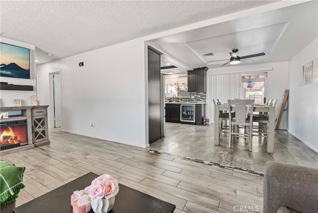 18396 Live Oak St, Hesperia, CA 92345 - living room featuring beverage cooler, a warm lit fireplace, wood tiled floors, a ceiling fan, and a textured ceiling