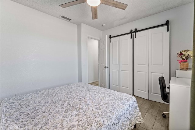 18396 Live Oak St, Hesperia, CA 92345 - bedroom featuring a textured ceiling, a barn door, light wood-style flooring, and a ceiling fan