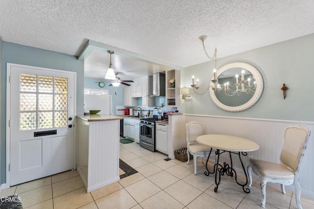 130 E Bay Blvd, Port Hueneme, CA 93041 - kitchen with stainless steel gas stove, wall chimney exhaust hood, a chandelier, wainscoting, and white cabinets