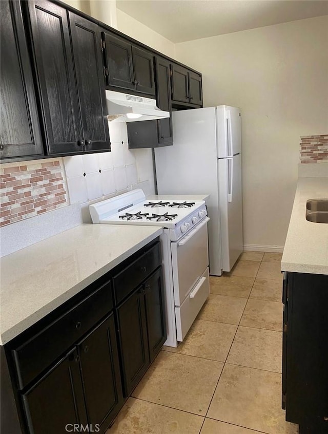 1303 W 109th Pl, Los Angeles, CA 90044 - kitchen featuring white range with gas stovetop, under cabinet range hood, dark cabinets, tasteful backsplash, and light tile patterned flooring