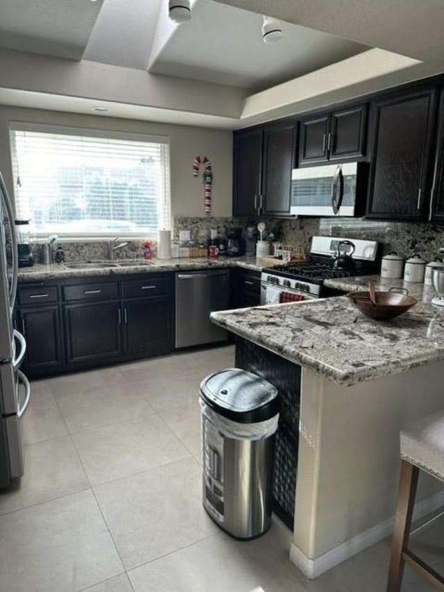 33878 Drifting Sands Cir, Thousand Palms, CA 92276 - kitchen with appliances with stainless steel finishes, a peninsula, light stone counters, and dark cabinets