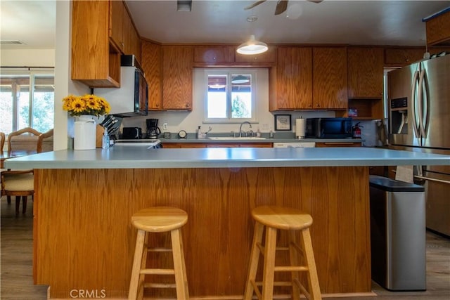 42179 High Point Ct, Ahwahnee, CA 93601 - kitchen with stainless steel refrigerator with ice dispenser, brown cabinetry, light countertops, black microwave, and light wood-style flooring