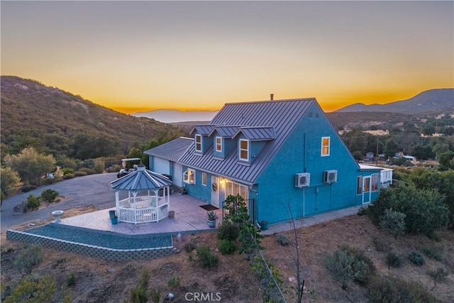 36227 Montezuma Valley Rd, Ranchita, CA 92066 - back of house at dusk featuring a standing seam roof, stucco siding, a metal roof, a deck with mountain view, and a gazebo