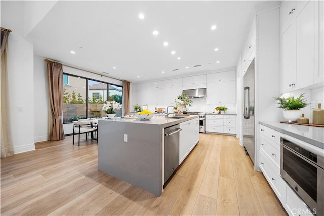 101 Lustro, Irvine, CA 92602 - kitchen with high end appliances, range hood, light wood-type flooring, backsplash, and a center island with sink