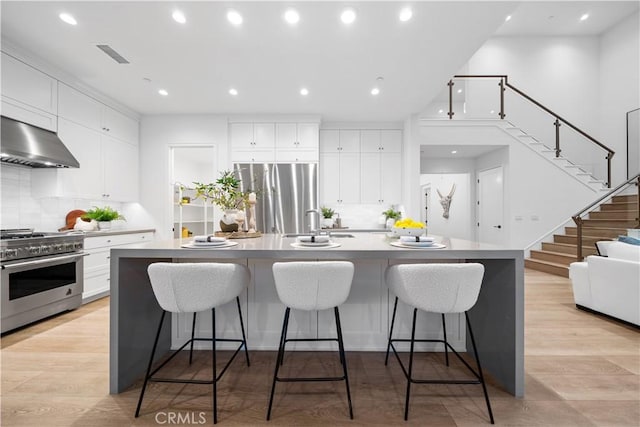 101 Lustro, Irvine, CA 92602 - kitchen featuring appliances with stainless steel finishes, ventilation hood, backsplash, a large island, and white cabinetry