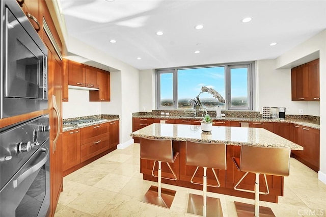 5124 Scholarship Unit 1007, Irvine, CA 92612 - kitchen with appliances with stainless steel finishes, a center island, brown cabinetry, recessed lighting, and a kitchen breakfast bar