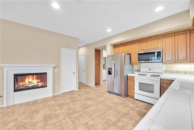 284 Tustin Field Dr, Tustin, CA 92782 - kitchen with appliances with stainless steel finishes, tile countertops, a glass covered fireplace, recessed lighting, and decorative backsplash