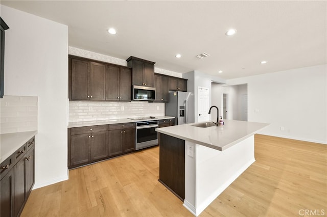28426 Joey Ct, Menifee, CA 92585 - kitchen featuring appliances with stainless steel finishes, dark brown cabinets, light wood finished floors, backsplash, and a center island with sink