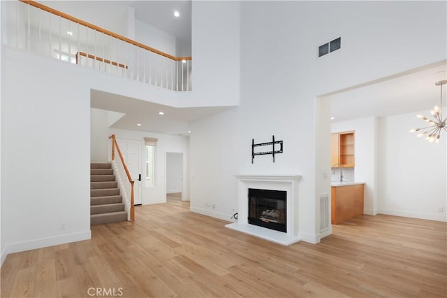 3 Longbourn Aisle, Irvine, CA 92603 - unfurnished living room featuring a high ceiling, stairway, light wood-type flooring, a chandelier, and a glass covered fireplace
