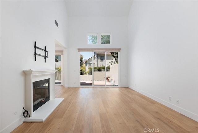 3 Longbourn Aisle, Irvine, CA 92603 - unfurnished living room featuring light wood-style flooring, a glass covered fireplace, and a towering ceiling