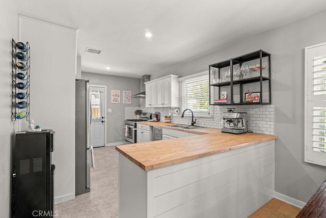 8213 Strub Ave, Whittier, CA 90602 - kitchen featuring stainless steel appliances, butcher block counters, tasteful backsplash, wall chimney exhaust hood, and a peninsula