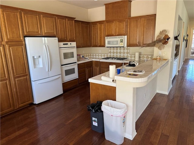 22045 Milestone St, Saugus, CA 91390 - kitchen featuring white appliances, brown cabinets, a peninsula, dark wood-style flooring, and tile counters