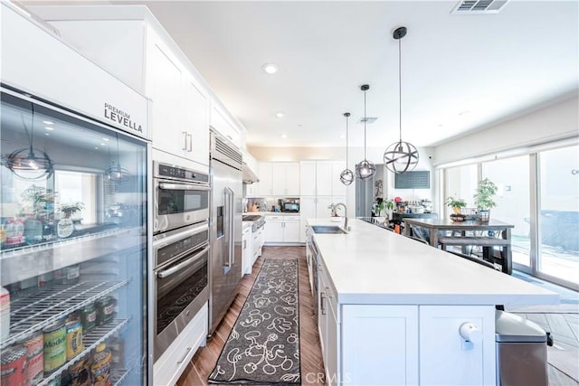 143 Interval, Irvine, CA 92618 - kitchen featuring stainless steel appliances, dark wood-style flooring, white cabinets, a center island with sink, and light countertops
