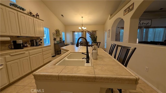 3242 Ashbury Ave, Madera, CA 93637 - kitchen with vaulted ceiling, light tile patterned flooring, a chandelier, a center island with sink, and a kitchen bar