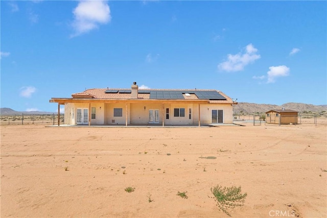 15090 Olema Rd, Apple Valley, CA 92307 - back of property with french doors, a mountain view, solar panels, stucco siding, and a chimney