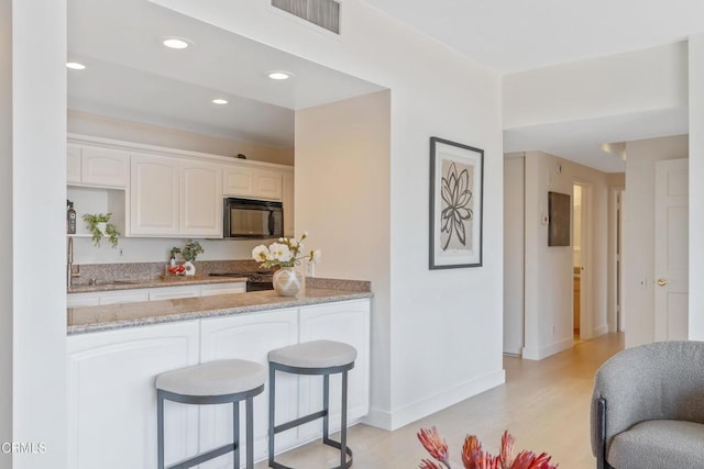 960 San Pasqual St Unit 208, Pasadena, CA 91106 - kitchen with black microwave, light stone counters, light wood-type flooring, white cabinets, and a peninsula