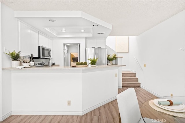 45 Briarglen Unit 64, Irvine, CA 92614 - kitchen featuring stainless steel appliances, light wood-style floors, a peninsula, a tray ceiling, and white cabinetry