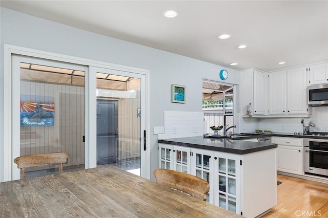 270 N Orange Grove Blvd, Pasadena, CA 91103 - kitchen featuring appliances with stainless steel finishes, dark countertops, decorative backsplash, white cabinetry, and light wood-type flooring