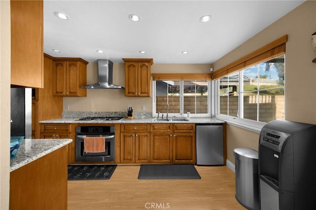 2405 E Alicia St, West Covina, CA 91792 - kitchen with wall chimney exhaust hood, black oven, brown cabinets, light wood finished floors, and light stone counters