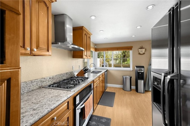 2405 E Alicia St, West Covina, CA 91792 - kitchen with wall chimney range hood, stainless steel appliances, light wood-type flooring, brown cabinetry, and light stone countertops