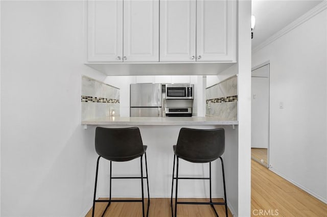 525 S Ardmore Ave Unit 257, Los Angeles, CA 90020 - kitchen with stainless steel appliances, a breakfast bar area, tasteful backsplash, ornamental molding, and light wood-style flooring