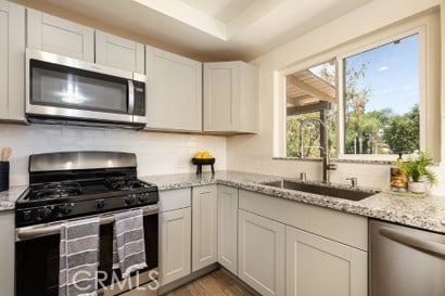 1939 S Broadway, Escondido, CA 92025 - kitchen featuring appliances with stainless steel finishes, wood finished floors, light stone counters, and decorative backsplash