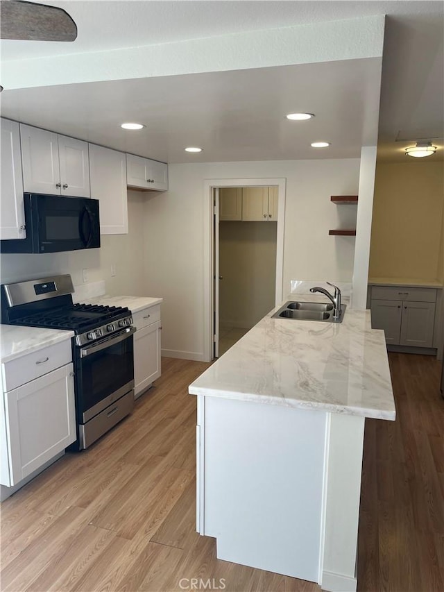 552 Canyon Dr Unit 38, Oceanside, CA 92054 - kitchen with black microwave, stainless steel range with gas cooktop, light wood-style floors, light stone counters, and white cabinetry