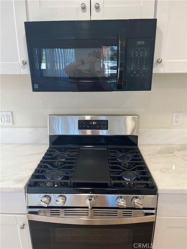 552 Canyon Dr Unit 38, Oceanside, CA 92054 - detailed view of stainless steel range with gas stovetop, black microwave, white cabinetry, and light stone counters