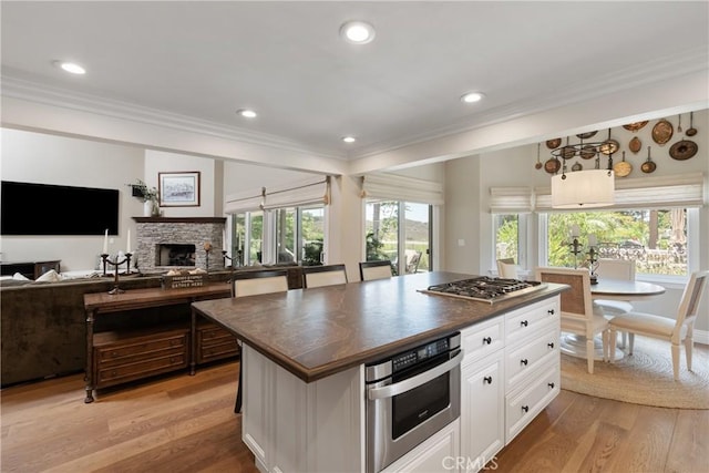 9911 Overhill Dr, North Tustin, CA 92705 - kitchen featuring crown molding, white cabinets, appliances with stainless steel finishes, light wood finished floors, and a stone fireplace