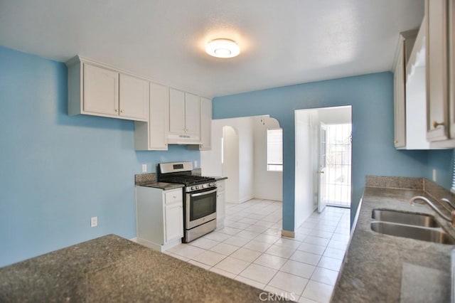 531 W 61st St, Los Angeles, CA 90044 - kitchen with gas range, under cabinet range hood, light tile patterned floors, dark countertops, and arched walkways