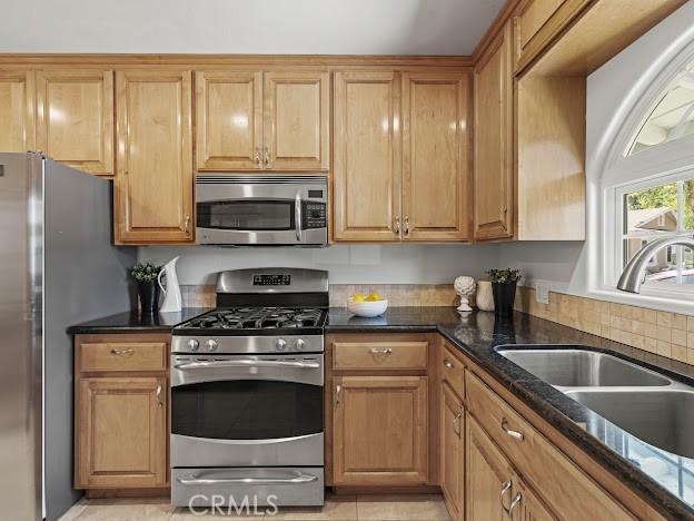 22601 Aguadero Pl, Saugus, CA 91350 - kitchen featuring stainless steel appliances, dark stone counters, brown cabinets, and light tile patterned floors