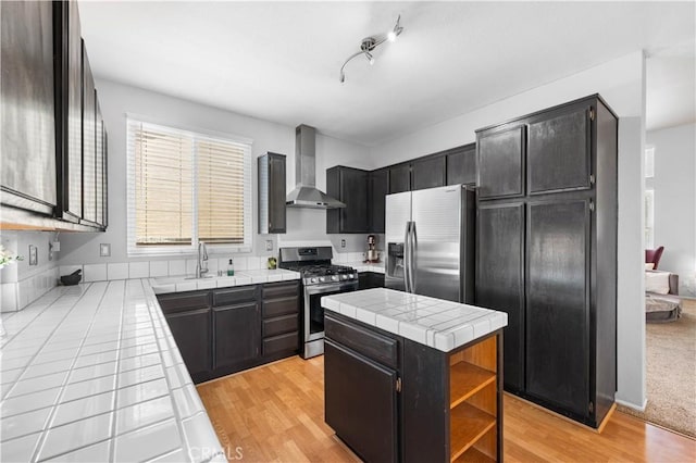 2659 Cold Creek Ave, Rosamond, CA 93560 - kitchen with appliances with stainless steel finishes, wall chimney exhaust hood, tile counters, a center island, and dark cabinetry