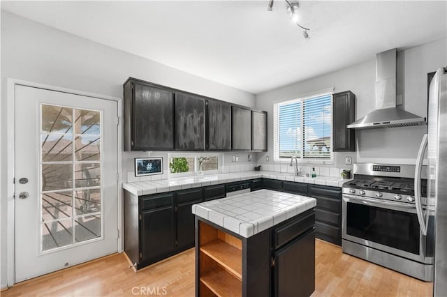 2659 Cold Creek Ave, Rosamond, CA 93560 - kitchen with wall chimney exhaust hood, stainless steel appliances, tile counters, and dark cabinets