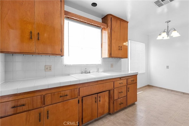 1256 Windsor Dr, San Bernardino, CA 92404 - kitchen with decorative backsplash, a chandelier, brown cabinetry, light flooring, and pendant lighting