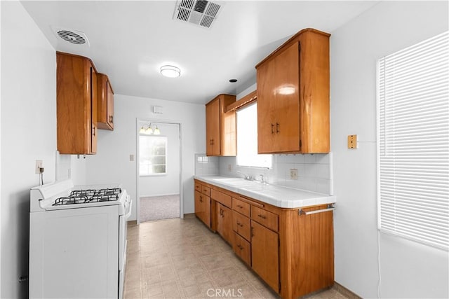1256 Windsor Dr, San Bernardino, CA 92404 - kitchen with white gas range, brown cabinetry, light flooring, and tasteful backsplash