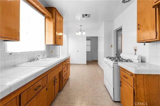 1256 Windsor Dr, San Bernardino, CA 92404 - kitchen featuring white gas stove, light flooring, tile countertops, decorative backsplash, and a chandelier
