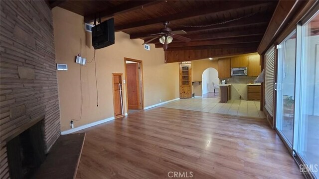 625 Cedar Ave, Wasco, CA 93280 - unfurnished living room featuring arched walkways, ceiling fan, a wooden ceiling with exposed beams, light wood finished floors, and a stone fireplace