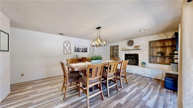 15233 Olive St, Hesperia, CA 92345 - dining space with wood finished floors, a textured ceiling, a stone fireplace, and a chandelier