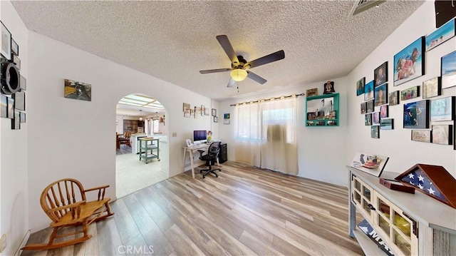 15233 Olive St, Hesperia, CA 92345 - home office featuring arched walkways, light wood finished floors, ceiling fan, and a textured ceiling