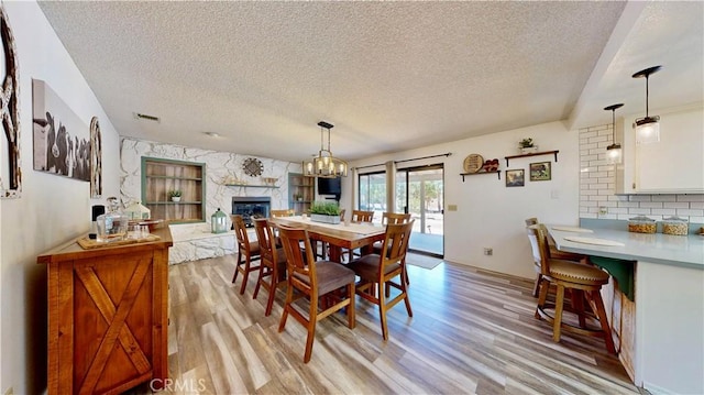 15233 Olive St, Hesperia, CA 92345 - dining space with light wood-style floors, a stone fireplace, a textured ceiling, and a chandelier