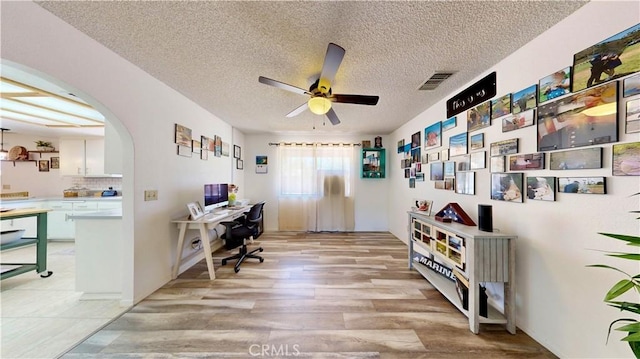 15233 Olive St, Hesperia, CA 92345 - home office with arched walkways, a ceiling fan, light wood finished floors, and a textured ceiling