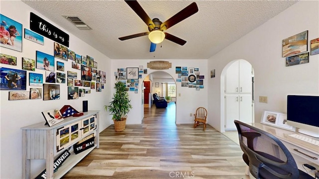 15233 Olive St, Hesperia, CA 92345 - home office featuring arched walkways, a ceiling fan, light wood-style flooring, and a textured ceiling