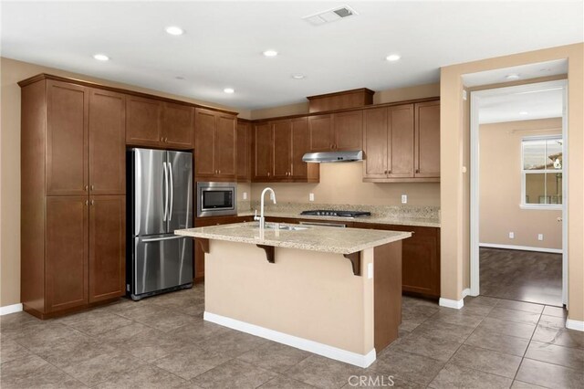 403 Sevilla Dr, Brea, CA 92823 - kitchen with stainless steel appliances, under cabinet range hood, a kitchen breakfast bar, light stone countertops, and an island with sink