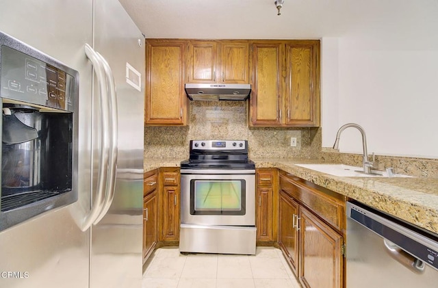 121 S Hope St Unit 321, Los Angeles, CA 90012 - kitchen with stainless steel appliances, under cabinet range hood, brown cabinetry, light tile patterned flooring, and tasteful backsplash