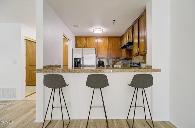 121 S Hope St Unit 321, Los Angeles, CA 90012 - kitchen featuring stainless steel refrigerator with ice dispenser, under cabinet range hood, light wood-style flooring, decorative backsplash, and a kitchen bar