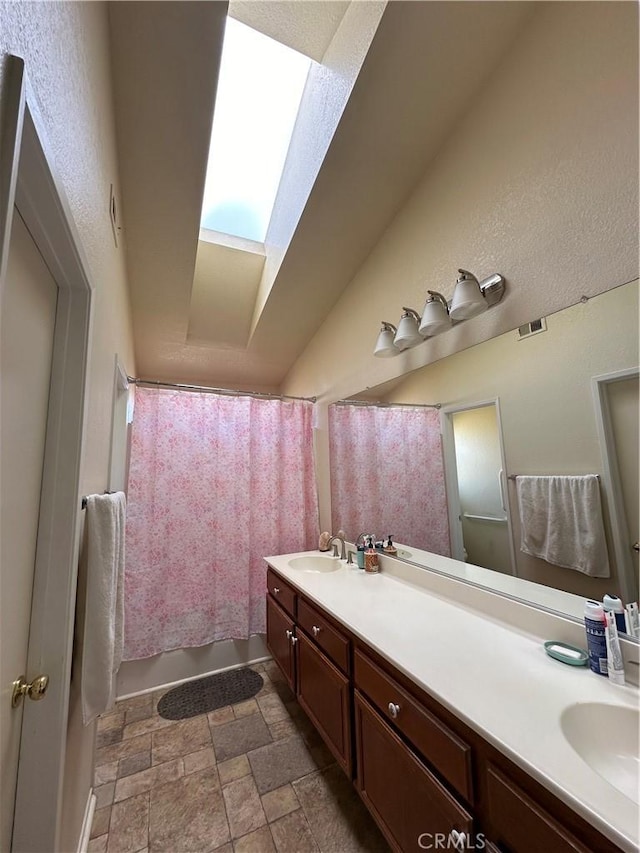 37510 Conifer Dr, Palmdale, CA 93550 - bathroom featuring double vanity, a skylight, stone finish flooring, and vaulted ceiling